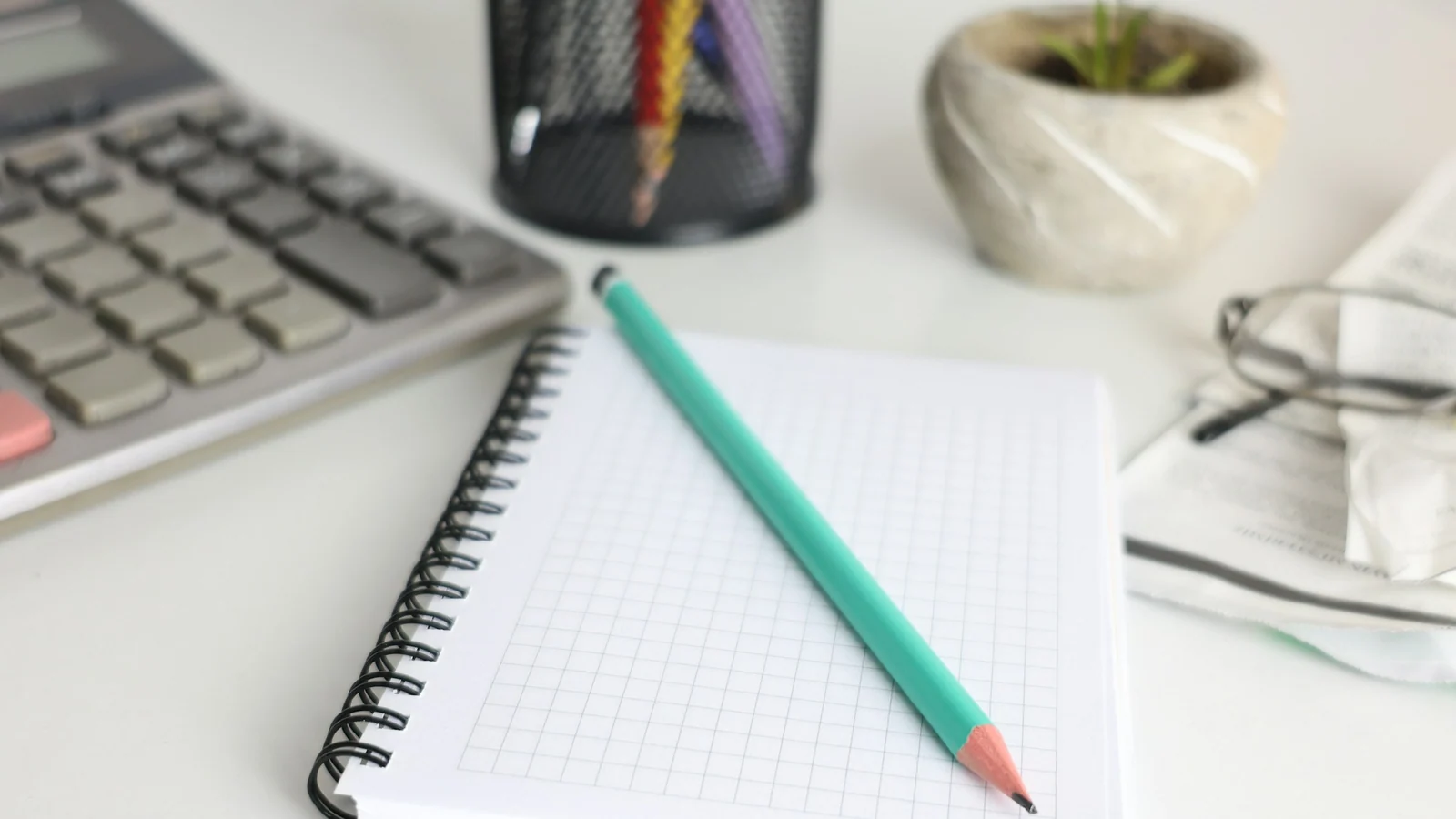 A budgeting workspace with a notebook, pencil, keyboard and small plant.