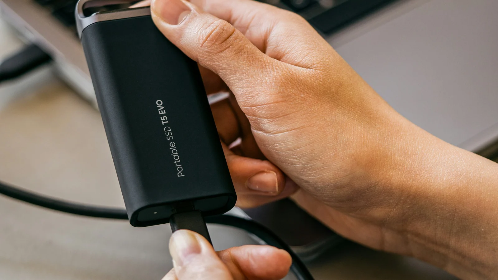 A person holds a portable solid-state drive beside a laptop.